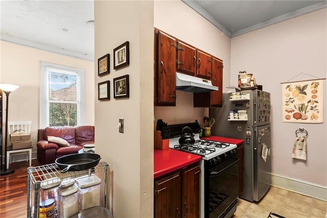 kitchen featuring under cabinet range hood, gas stove, baseboards, and ornamental molding