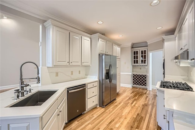 kitchen with sink, white cabinetry, light wood-type flooring, ornamental molding, and appliances with stainless steel finishes