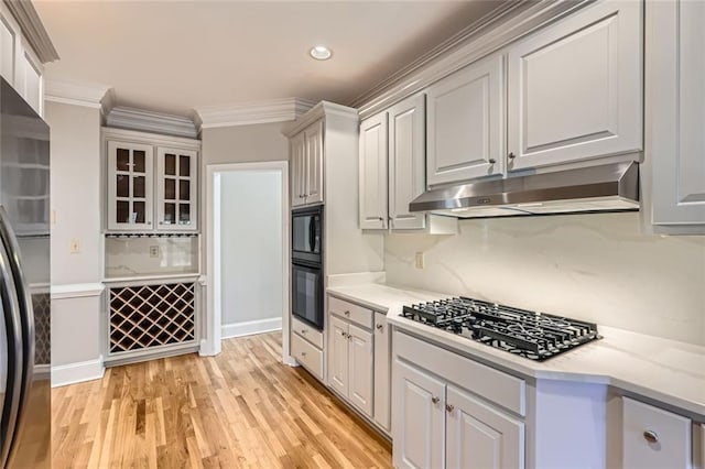 kitchen with white cabinets, decorative backsplash, ornamental molding, black appliances, and light wood-type flooring