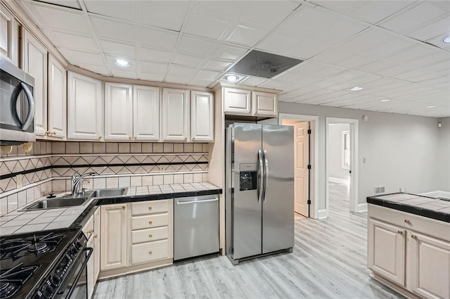 kitchen with sink, decorative backsplash, tile counters, stainless steel appliances, and light hardwood / wood-style flooring