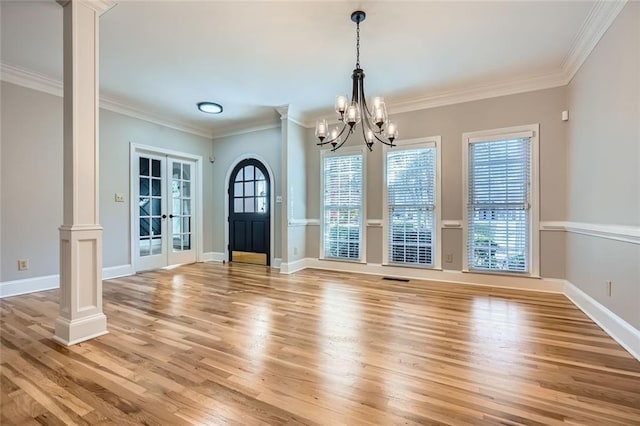 unfurnished dining area featuring french doors, light hardwood / wood-style floors, decorative columns, and a wealth of natural light