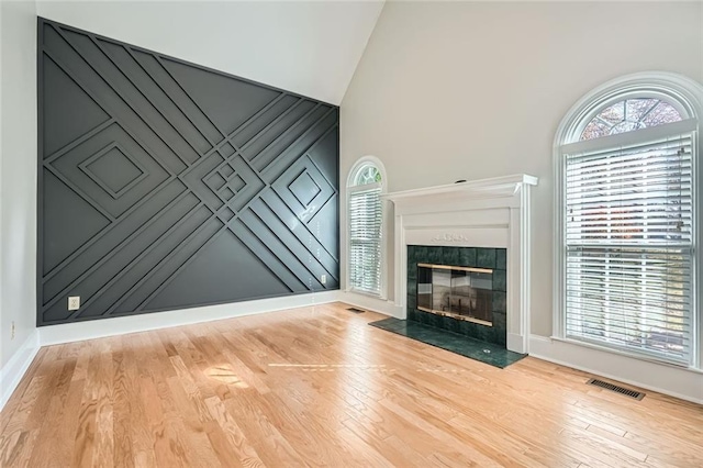 unfurnished living room with a tiled fireplace, high vaulted ceiling, and light hardwood / wood-style flooring