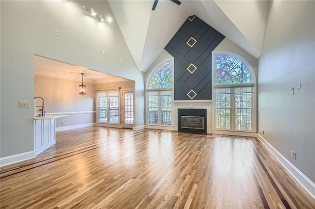 unfurnished living room featuring ornamental molding, ceiling fan, high vaulted ceiling, and light hardwood / wood-style floors