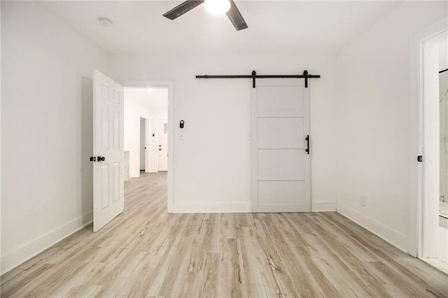 spare room with ceiling fan, a barn door, and light wood-type flooring