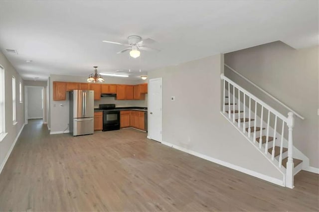 kitchen with ceiling fan with notable chandelier, stainless steel refrigerator, black electric range oven, light wood-type flooring, and range hood