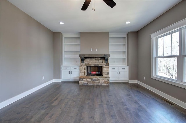 unfurnished living room with baseboards, visible vents, dark wood finished floors, and a stone fireplace