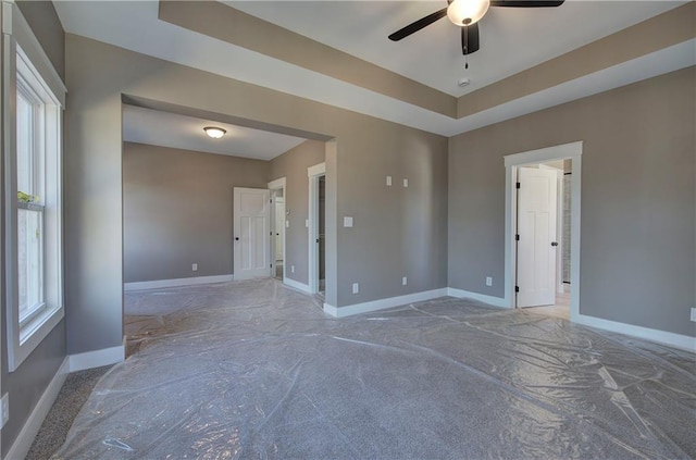 unfurnished room featuring plenty of natural light, a raised ceiling, a ceiling fan, and baseboards