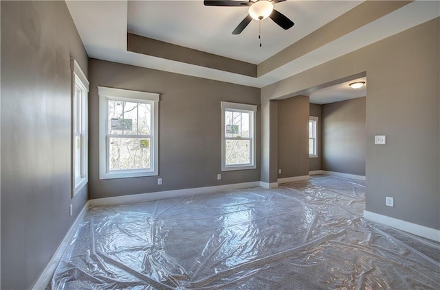 spare room with ceiling fan, a tray ceiling, and baseboards