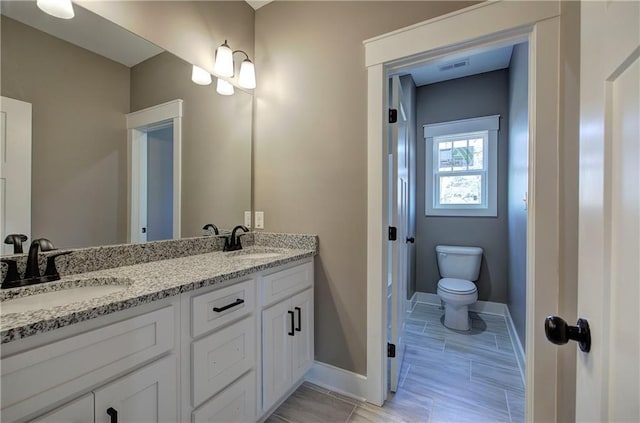 bathroom with double vanity, a sink, toilet, and baseboards