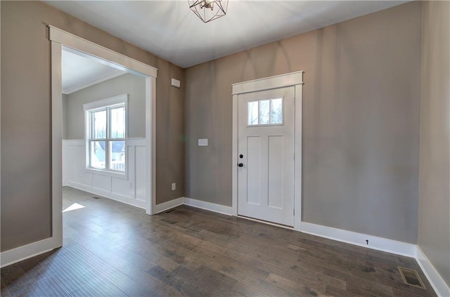 foyer entrance featuring a decorative wall, a wainscoted wall, visible vents, baseboards, and dark wood finished floors