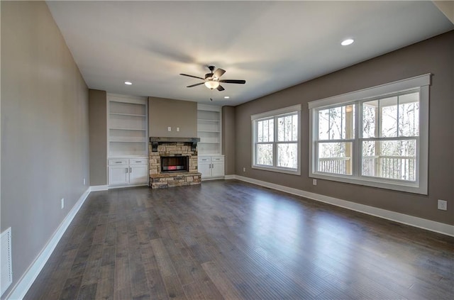 unfurnished living room with baseboards, dark wood finished floors, a ceiling fan, a stone fireplace, and recessed lighting