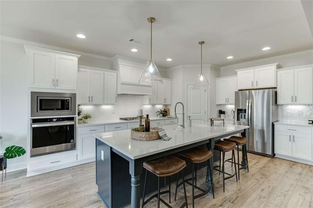 kitchen with a breakfast bar area, appliances with stainless steel finishes, white cabinetry, a kitchen island with sink, and decorative light fixtures