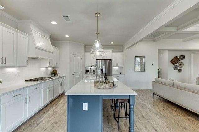 kitchen with appliances with stainless steel finishes, beamed ceiling, sink, white cabinets, and a center island with sink