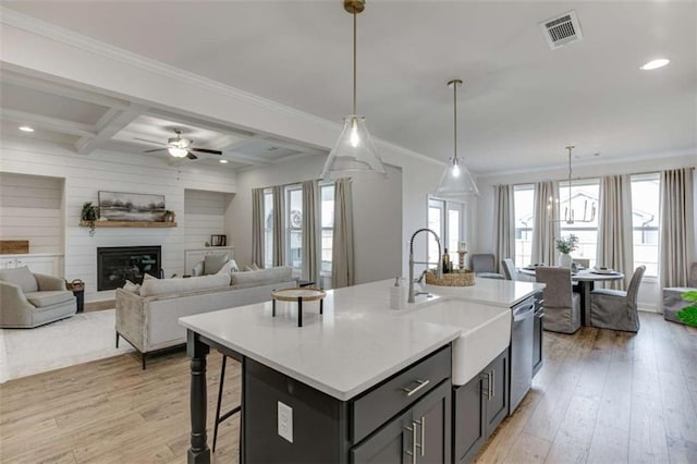 kitchen featuring sink, a kitchen island with sink, coffered ceiling, decorative light fixtures, and beamed ceiling