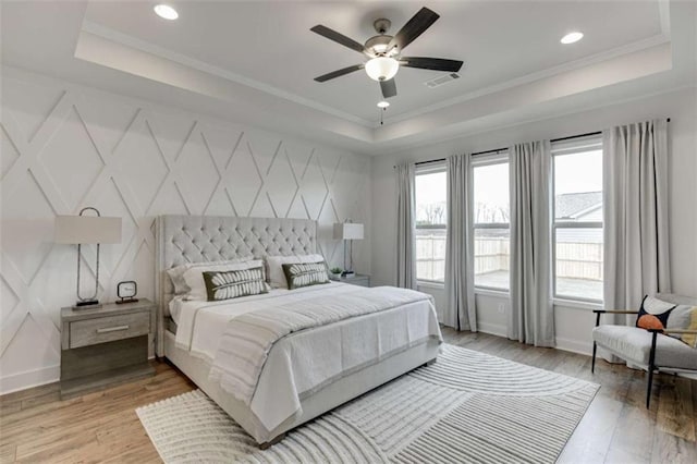 bedroom with a tray ceiling, ceiling fan, and light wood-type flooring