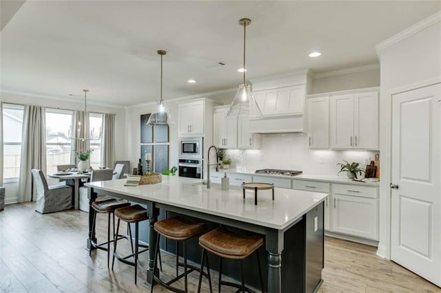 kitchen with white cabinetry, a kitchen breakfast bar, an island with sink, pendant lighting, and stainless steel appliances