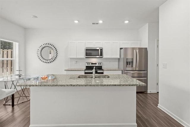 kitchen with dark hardwood / wood-style flooring, appliances with stainless steel finishes, a kitchen island with sink, white cabinetry, and light stone counters