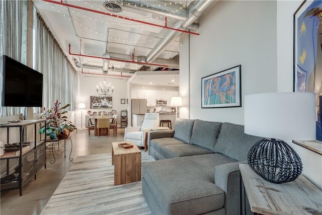 living area with light wood-type flooring, visible vents, a notable chandelier, and a high ceiling