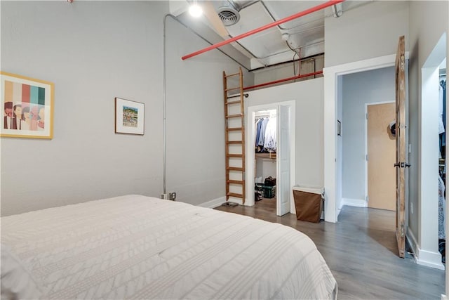 bedroom with dark wood-style flooring, visible vents, baseboards, a closet, and a walk in closet