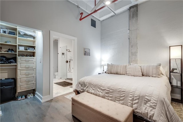 bedroom with a towering ceiling, light wood-style flooring, baseboards, and connected bathroom