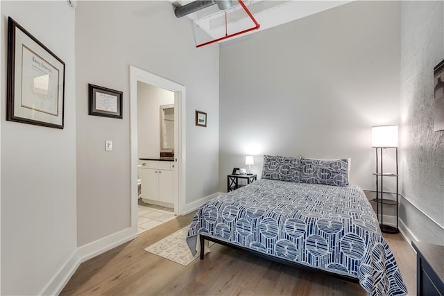 bedroom featuring connected bathroom, a high ceiling, baseboards, and wood finished floors