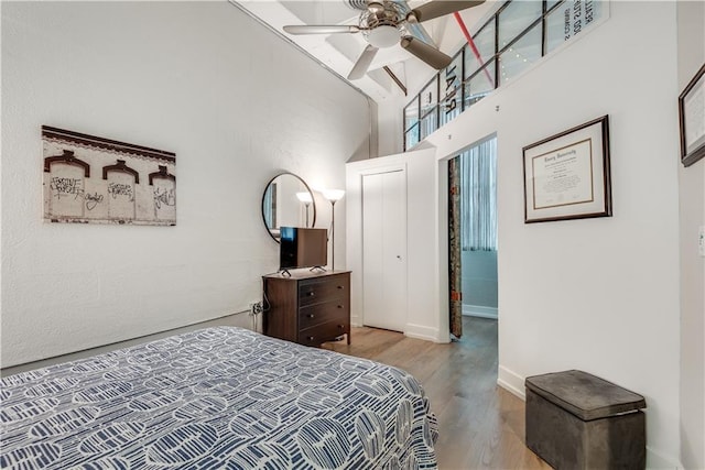 bedroom featuring baseboards, ceiling fan, light wood-style flooring, and a towering ceiling