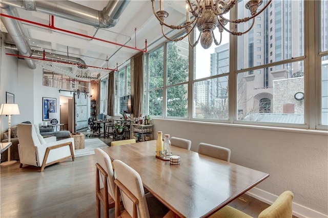 dining space featuring a barn door, baseboards, wood finished floors, an inviting chandelier, and a high ceiling