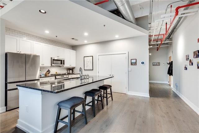 kitchen featuring dark stone counters, a spacious island, appliances with stainless steel finishes, a breakfast bar, and white cabinetry