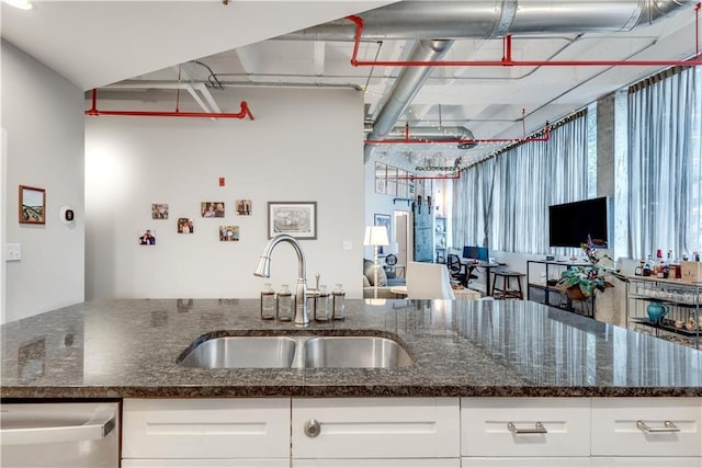 kitchen featuring dark stone counters, white cabinets, a sink, and stainless steel dishwasher