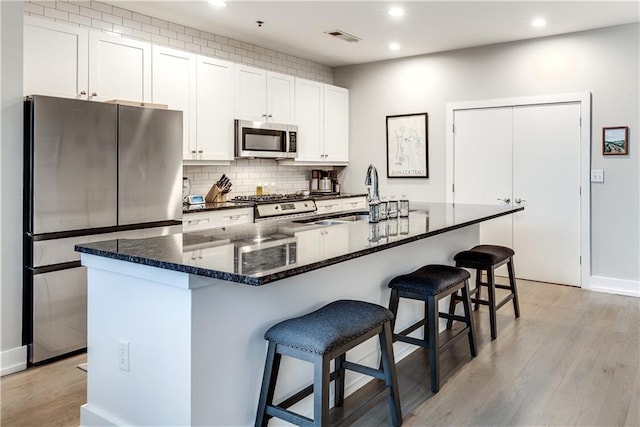 kitchen featuring white cabinets, a kitchen island with sink, visible vents, and stainless steel appliances