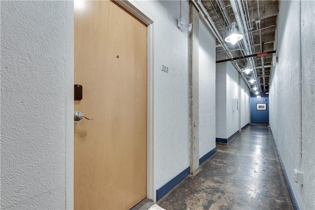 hall featuring concrete flooring and a textured wall