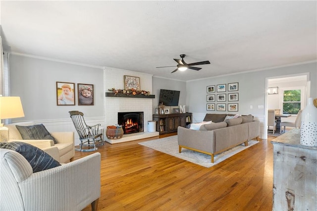 living room featuring a fireplace, wood-type flooring, ceiling fan, and ornamental molding