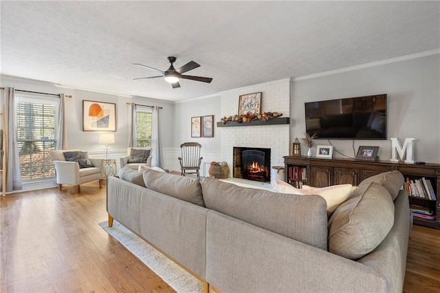 living room featuring hardwood / wood-style floors, a fireplace, ceiling fan, and crown molding