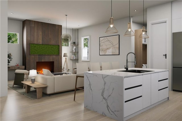 kitchen featuring white cabinets, an island with sink, sink, and a large fireplace