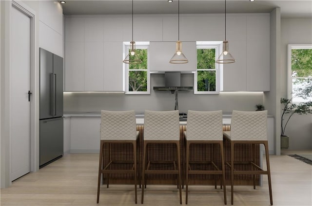 kitchen with stainless steel refrigerator, light wood-type flooring, a kitchen breakfast bar, decorative light fixtures, and white cabinetry