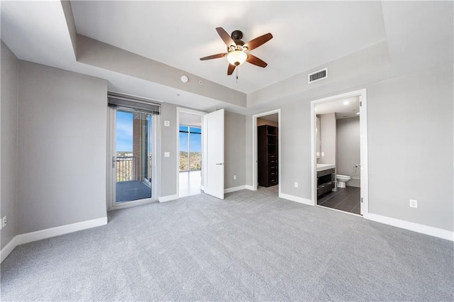 unfurnished bedroom with access to exterior, a tray ceiling, carpet, visible vents, and baseboards