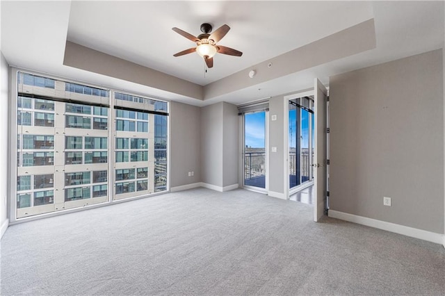 spare room featuring carpet floors, a tray ceiling, and baseboards