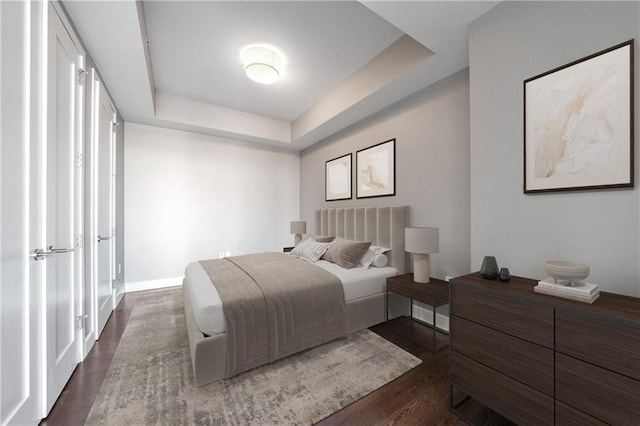 bedroom with dark wood-type flooring, a raised ceiling, and baseboards