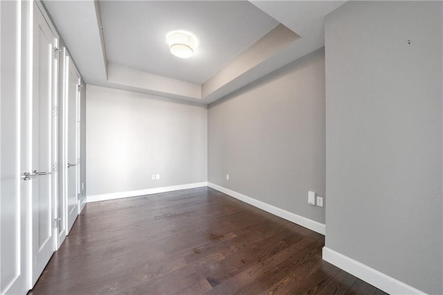 empty room featuring a tray ceiling, dark wood-style flooring, and baseboards