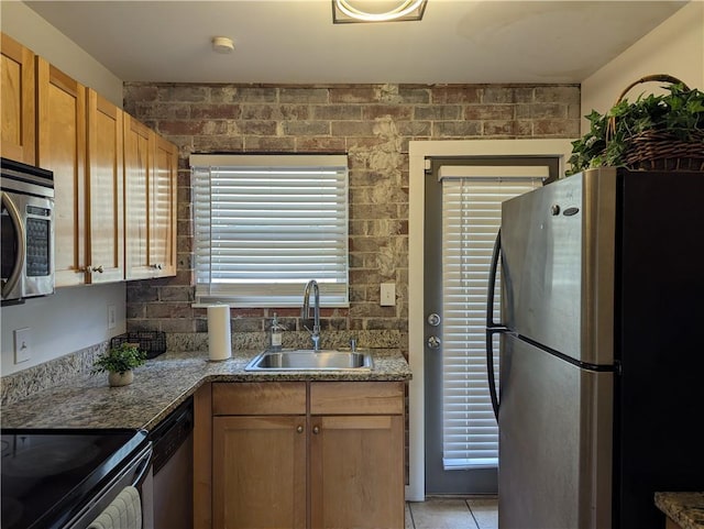 kitchen with light stone counters, appliances with stainless steel finishes, brown cabinets, a sink, and light tile patterned flooring