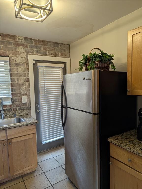 kitchen featuring light tile patterned floors, dark stone counters, a sink, and freestanding refrigerator