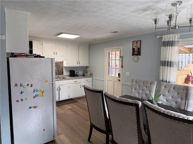 kitchen featuring stainless steel refrigerator, sink, white cabinets, dark hardwood / wood-style flooring, and a textured ceiling