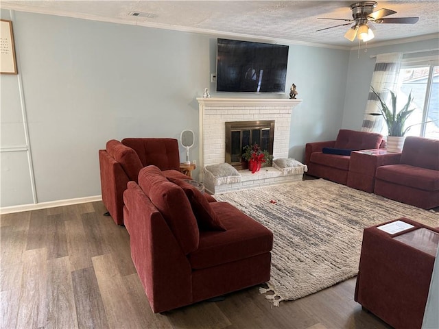 living room with a textured ceiling, ornamental molding, dark hardwood / wood-style flooring, ceiling fan, and a fireplace