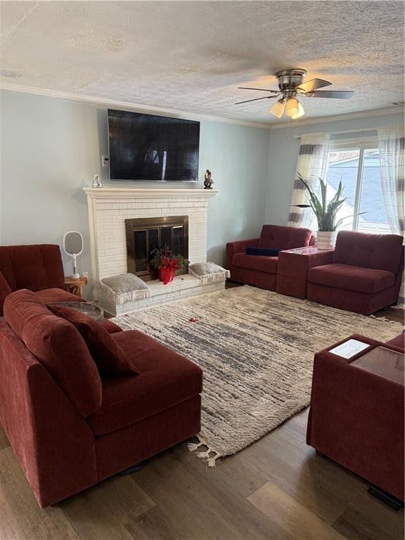 living room featuring a fireplace, wood-type flooring, ceiling fan, crown molding, and a textured ceiling