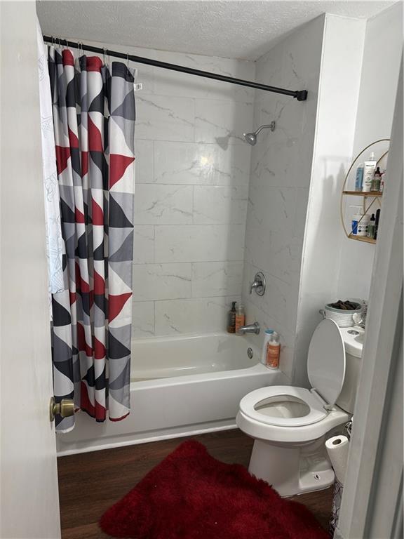 bathroom with hardwood / wood-style flooring, toilet, shower / bath combination with curtain, and a textured ceiling