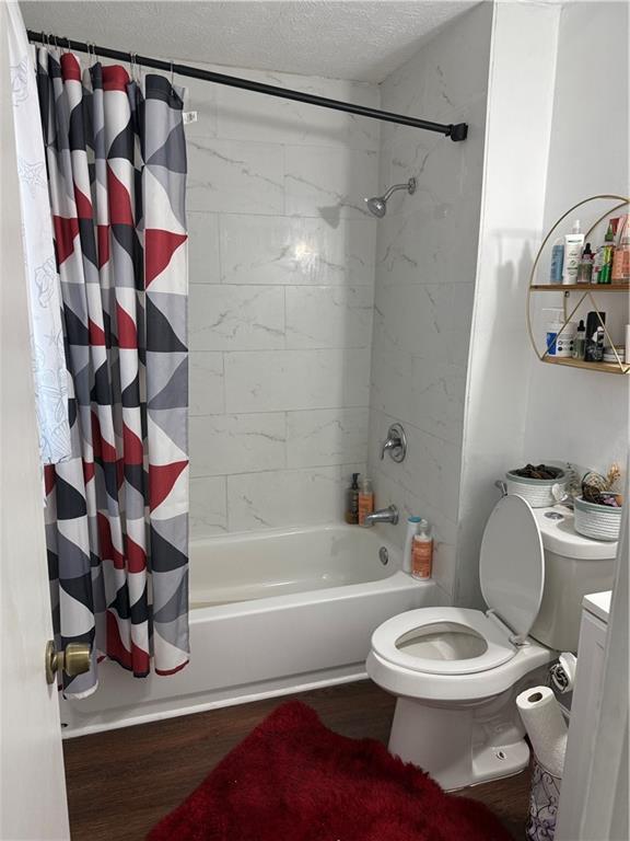 bathroom featuring hardwood / wood-style floors, shower / bath combination with curtain, a textured ceiling, and toilet