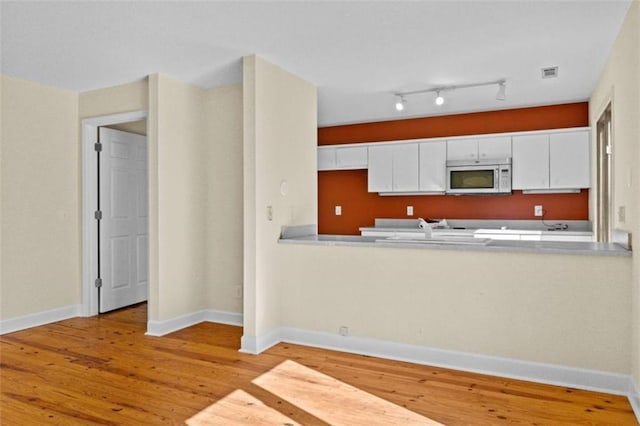 kitchen featuring white microwave, light wood-style flooring, visible vents, white cabinets, and light countertops