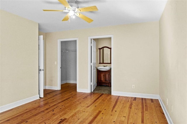 unfurnished bedroom with a closet, baseboards, wood finished floors, a walk in closet, and a sink