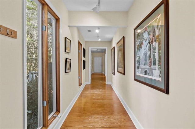 hall featuring light wood finished floors, baseboards, and rail lighting