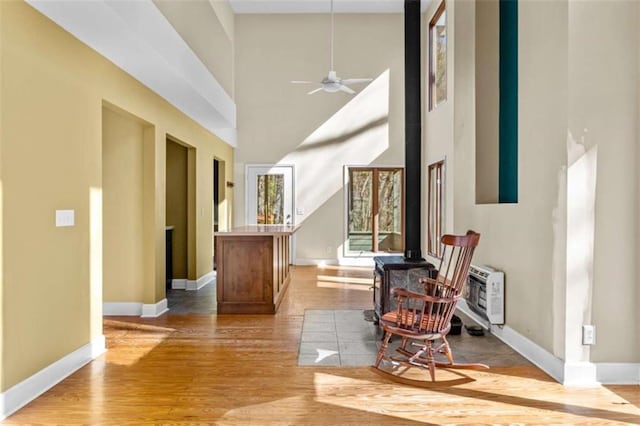 entryway with light wood-style flooring, a ceiling fan, a wood stove, and baseboards